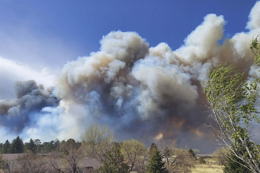 Smoke from a wind-whipped wildfire rises above neighborhoods on the outskirts of Flagstaff, Ariz., on Tuesday, April 19, 2022. Homes on the outskirts of Flagstaff were being evacuated Tuesday as high winds whipped a wildfire, shut down a major highway and grounded firefighting aircraft.