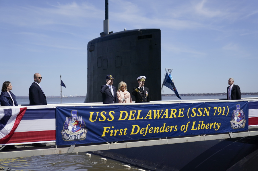 President Joe Biden returns a salute as he stands with first lady Jill Biden and Cmdr. Matthew Horton, Commanding Officer, USS Delaware, before they board the USS Delaware, Virginia-class fast-attack submarine, for a tour at the Port of Wilmington in Wilmington, Del., Saturday, April 2, 2022.