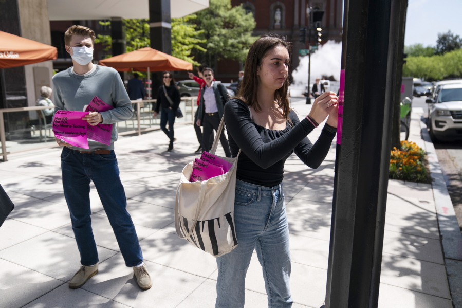 George Washington University student Kai Nilsen, left, watches as American University student Magnolia Mead as they put up posters near the White House promoting student loan debt forgiveness, Friday, April 29, 2022, in Washington.