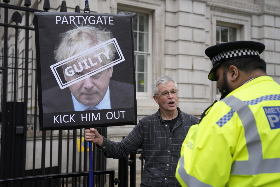 A police officer talks to a protester holding up a sign showing British Prime Minister Boris Johnson, in front of the entrance to Downing Street in London, Wednesday, April 13, 2022. Johnson was fined for breaching COVID-19 regulations following allegations of lockdown parties at government offices.