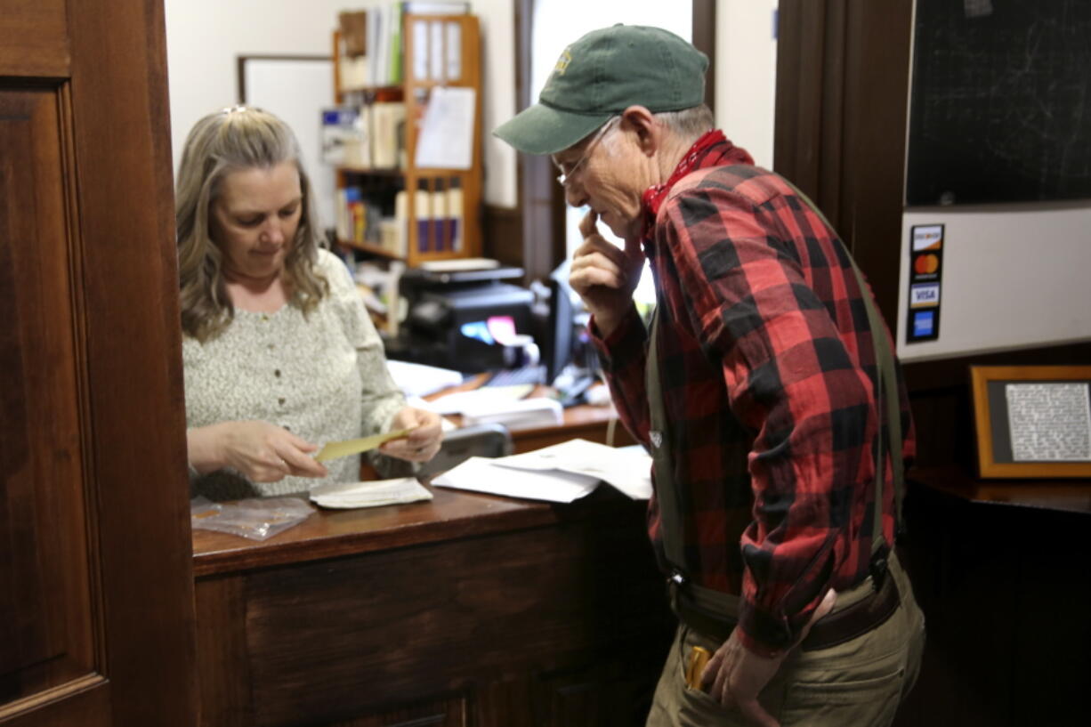 Victory Town Clerk Tracey Martel, left, helps town resident Will Staats buy dog licenses in Victory, Vt., Thursday, March 31, 2022. Martel says she's regularly frustrated watching a spinning circle on her computer while she tries to complete even the most basic municipal chores online. It could be years before high-speed internet reaches Victory. The need to connect homes and businesses to high-speed broadband services was highlighted by the COVID-19 pandemic and officials say that while there is lots of money available, supply and labor shortages are making the expansion a challenge.