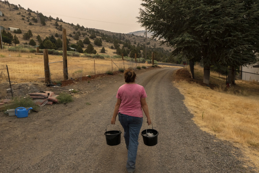 FILE - Misty Buckley carries dirty water from her animals' pens to water plants in her front yard, Saturday, July 24, 2021, in Klamath Falls, Ore. Farms that rely on irrigation from a depleted, federally managed lake on the California-Oregon border, along with a Native American tribe fighting to protect fragile salmon, will both receive greatly reduced amounts of water again in the summer of 2022 as a historic drought and record-low reservoir levels drag on in the U.S. West.