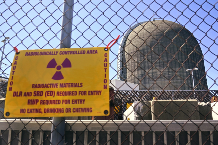 FILE-- A sign warning of radioactive materials is seen on a fence around a nuclear reactor containment building on Monday, April 26, 2021, a few days before it stopped generating electricity at Indian Point Energy Center in Buchanan, N.Y. The Biden administration is launching a $6 billion effort to save nuclear power plants at risk of closing, citing the need to continue nuclear energy as a carbon-free source of power that helps to combat climate change.