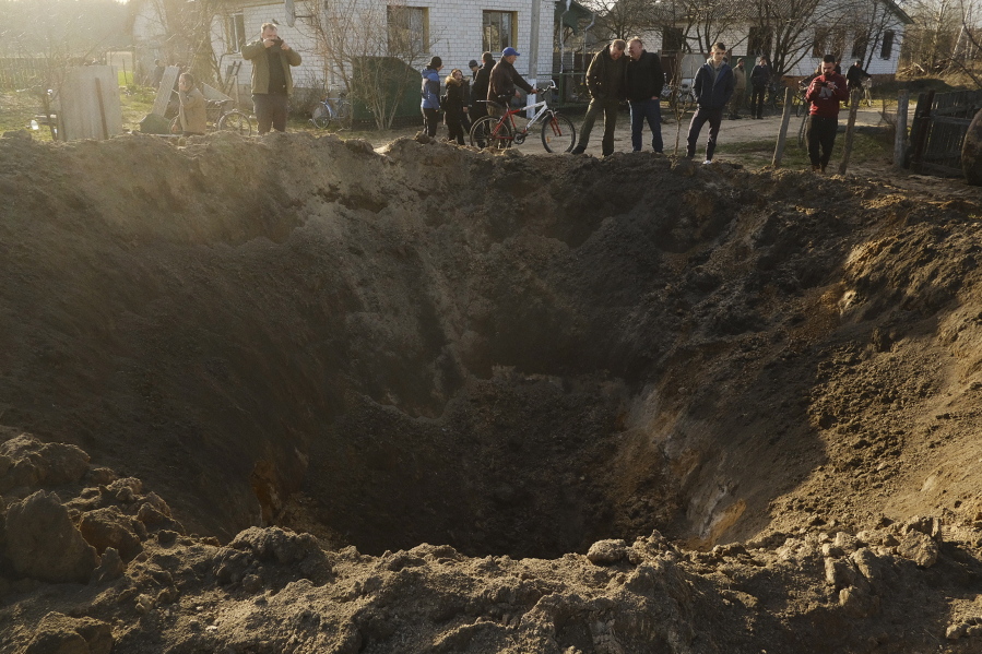 People look at a crater of an explosion in a village of Horodnya, Chernihiv region, Ukraine, Thursday, April 14, 2022. The fluid nature of the conflict, which has seen fighting shift away from areas around the capital and heavily toward Ukraine's east, has made the task of reaching hungry Ukrainians especially difficult.