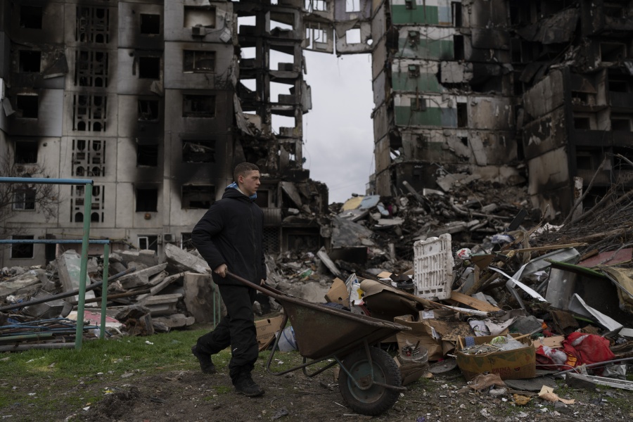 A young man pushes a wheelbarrow in front of a destroyed apartment building in the town of Borodyanka, Ukraine, on Sunday, April 10, 2022. Several apartment buildings were destroyed during fighting between the Russian troops and the Ukrainian forces and the town is without electricity, water and heating.