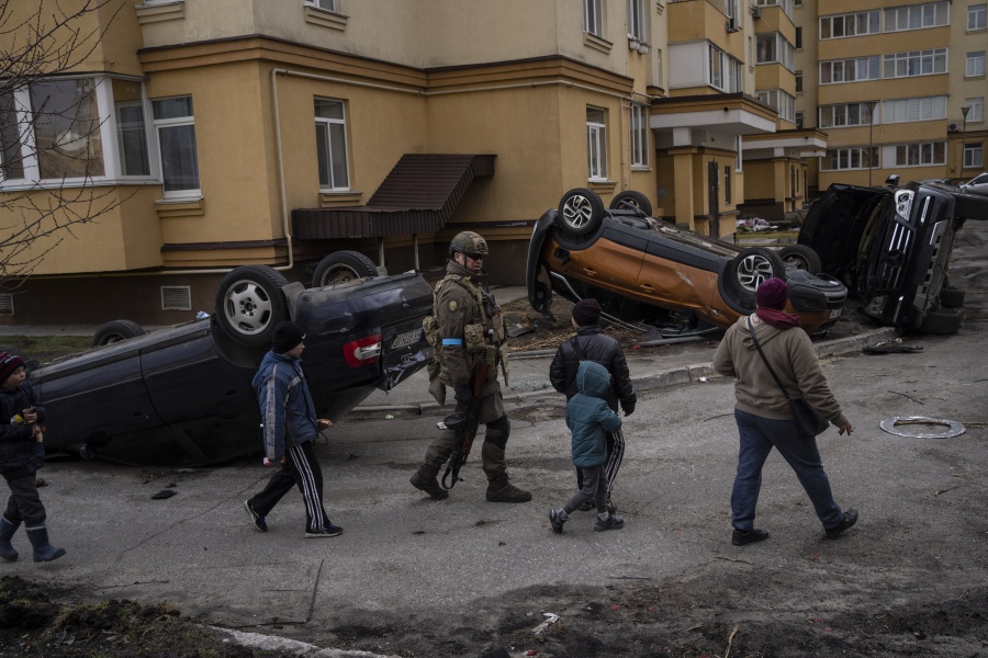 A Ukrainian soldier walks with children passing destroyed cars due to the war against Russia, in Bucha, on the outskirts of Kyiv, Ukraine, Monday, April 4, 2022.