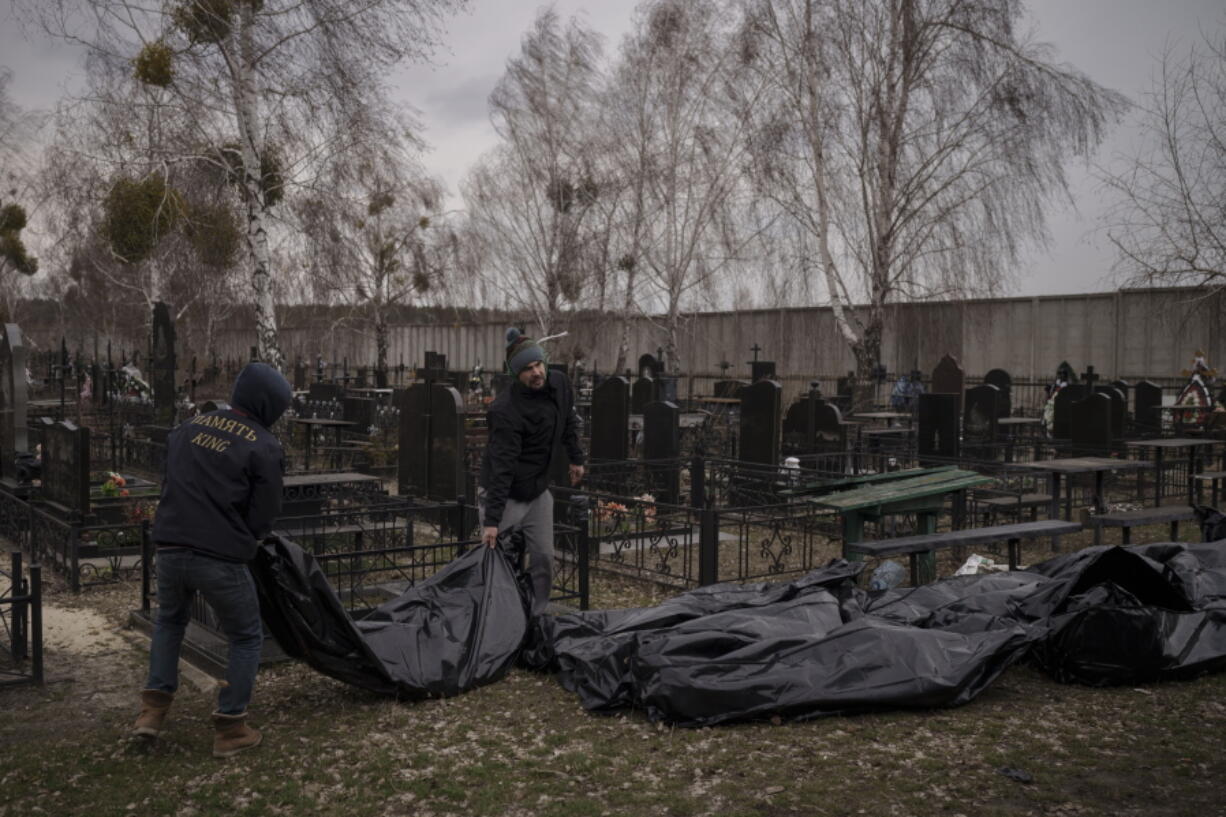 Workers carry the body of people found dead to a cemetery in Bucha, outskirts of Kyiv, Ukraine, Tuesday, April 5, 2022. Ukraine's president told the U.N. Security Council on Tuesday that the Russian military must be brought to justice immediately for war crimes, accusing invading troops of the worst atrocities since World War II. He stressed that Bucha was only one place and there are more with similar horrors.