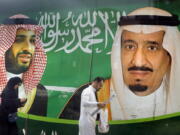 FILE - People walk past a banner showing Saudi King Salman, right, and his Crown Prince Mohammed bin Salman, outside a mall in Jiddah, Saudi Arabia, Saturday, March 7, 2020. A spike in global energy prices caused by Russia's war on Ukraine benefits Saudi Arabia as the world's top oil exporter, but problems remain for the kingdom's impulsive crown prince.