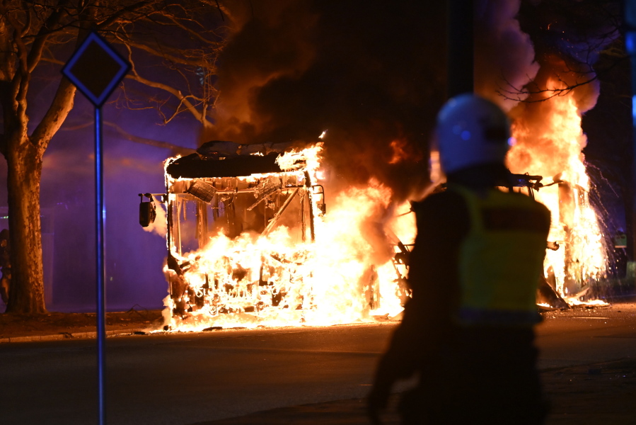 Riot police watch a city bus burn on a street in Malmo, Sweden, Saturday, April 16, 2022. Unrest broke out in southern Sweden late Saturday despite police moving a rally by an anti-Islam far-right group, which was planning to burn a Quran among other things, to a new location as a preventive measure.