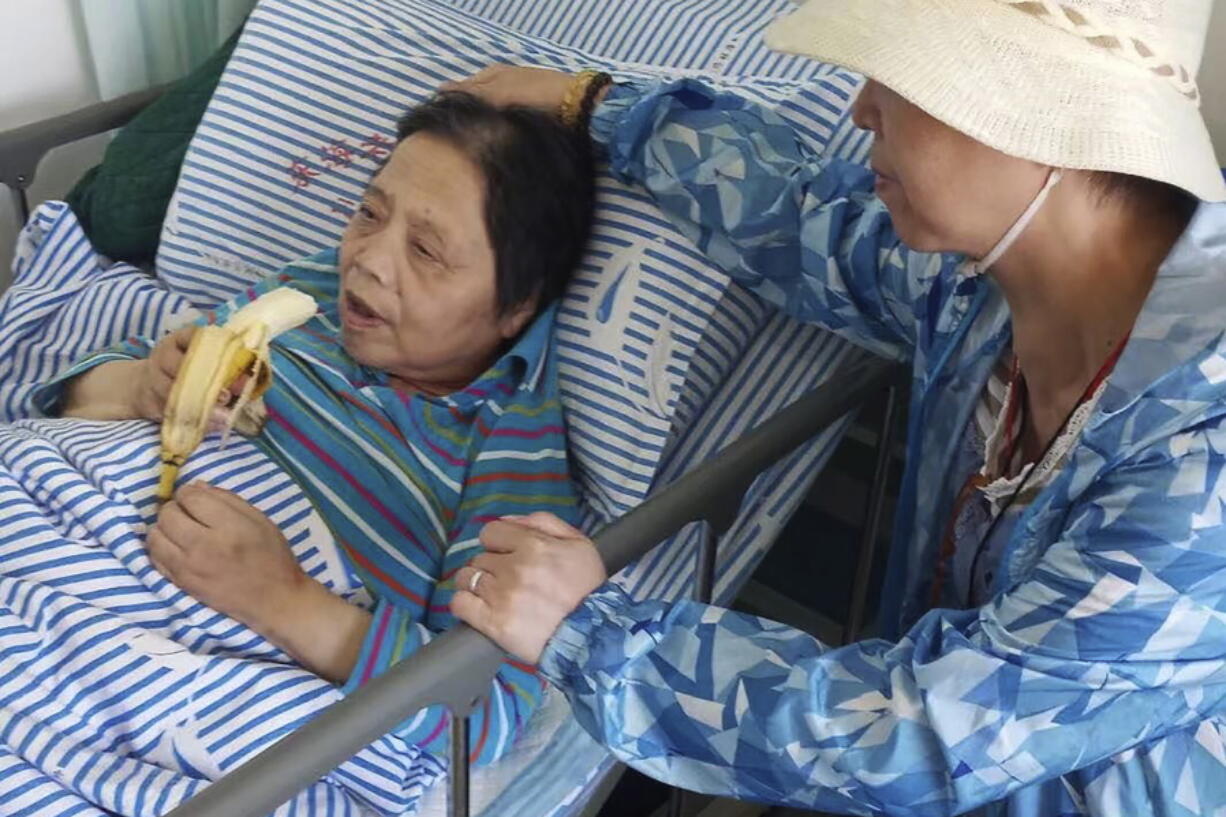 In this photo released by the family of Shen Peiming, Shen Peiming, 71, eats a banana as a family member attends to her at her bed side at the Shanghai Donghai Elderly Care hospital on Sept. 24, 2019.  Shen died  Sunday morning, April 3, 2022, at the hospital, without her loved ones by her side. Her family, unable to visit because of pandemic restrictions, is unsure of the circumstances of her death. The hospital had reported a COVID-19 outbreak, but Shen had tested negative, as of last week.