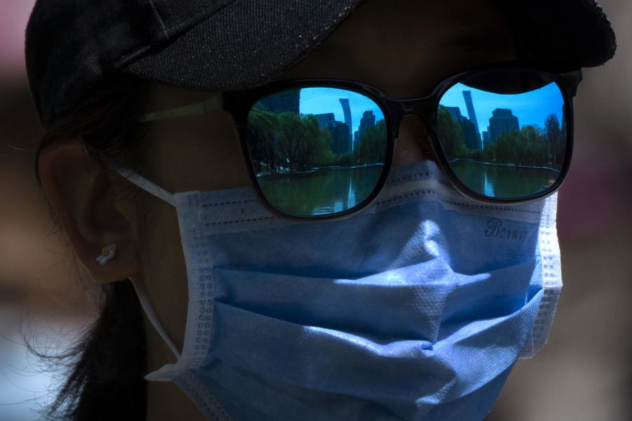 The skyline of Beijing is reflecting in the sunglasses of a woman wearing a face mask as she walks at a public park in Beijing, Thursday, April 14, 2022.