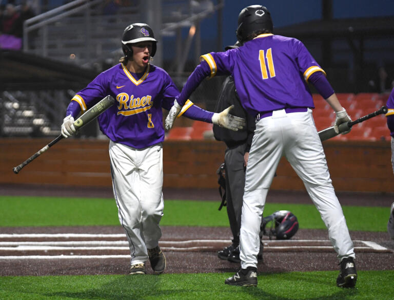 Columbia River junior Austin Habets, left, celebrates with senior Henry Palmersheim after scoring a run Wednesday, May 11, 2022, during the Rapids’ 9-4 win against W.F. West in a 2A district semifinal game at the Ridgefield Outdoor Recreation Complex.