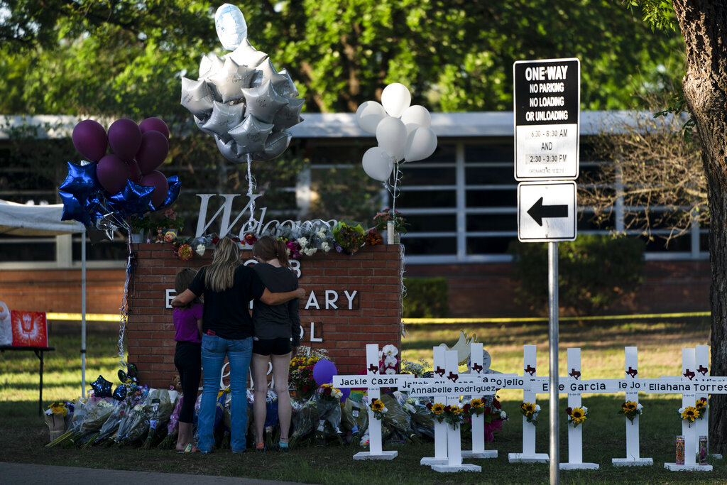 A family pays their respects next to crosses bearing the names of Tuesday's shooting victims at Robb Elementary School in Uvalde, Texas, Thursday, May 26, 2022. (AP Photo/Jae C.