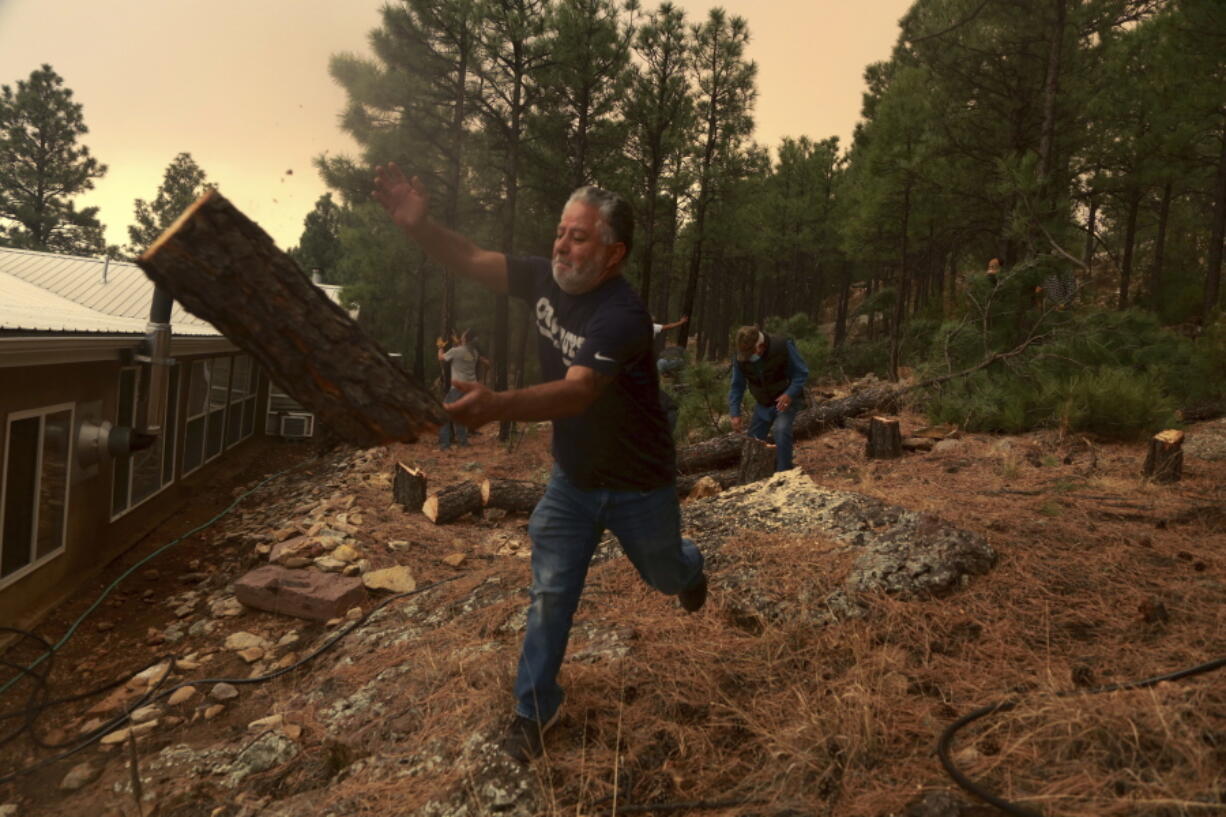 Chris Castillo throws a freshly-cut log as he and his cousins clear a wireline along a family member's home in Las Vegas, N.M., Monday, May 2, 2022. Wind-whipped flames are marching across more of New Mexico's tinder-dry mountainsides, forcing the evacuation of area residents and dozens of patients from the state's psychiatric hospital as firefighters scramble to keep new wildfires from growing.