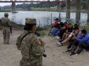 Migrants who had crossed the Rio Grande river into the U.S. are under custody of National Guard members as they await the arrival of U.S. Border Patrol agents in Eagle Pass, Texas, Friday, May 20, 2022. The Eagle Pass area has become increasingly a popular crossing corridor for migrants, especially those from outside Mexico and Central America, under Title 42 authority, which expels migrants without a chance to seek asylum on grounds of preventing the spread of COVID-19. A judge was expected to rule on a bid by Louisiana and 23 other states to keep Title 42 in effect before the Biden administration was to end it Monday.