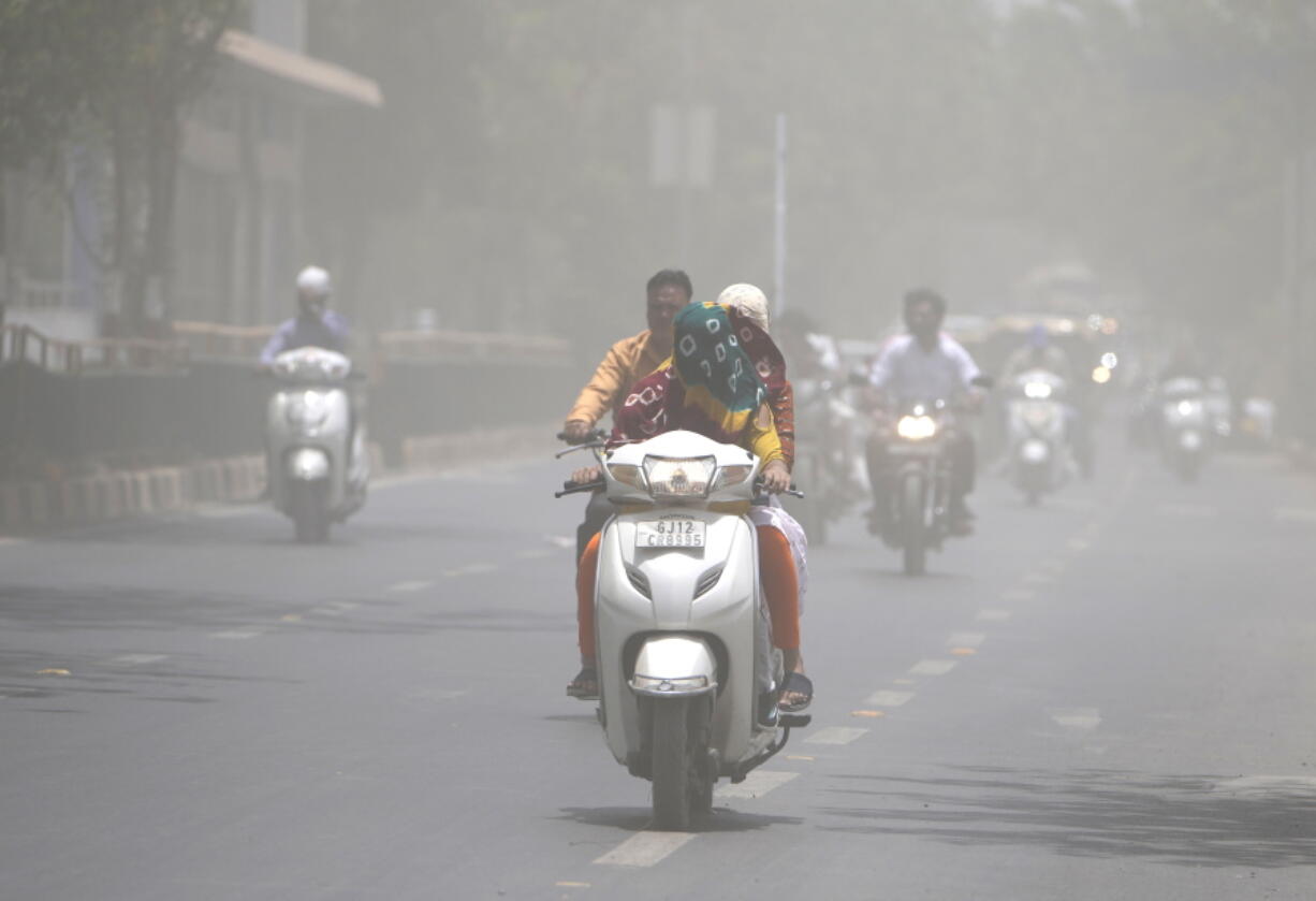 A woman covers her face with a scarf to protect from heat wave rides through a dust storm in Ahmedabad, India, on Saturday.