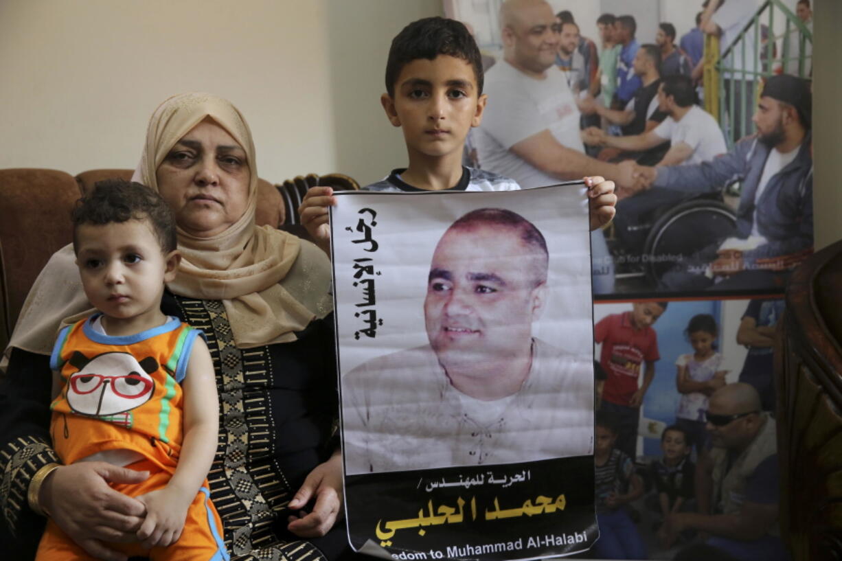 FILE - Amal el-Halabi holds her grandson Fares while her grandson Amro, 7, holds a picture of his father Mohammed el-Halabi, Gaza director of the international charity World Vision, who is detained and accused by Israeli security of diverting sums to Hamas that exceed its total budget, at his family house in Gaza City, Aug. 8, 2016. In May 2022, nearly six years after Israel accused Mohammed el-Halabi of diverting tens of millions of dollars from an international charity to Gaza's militant Hamas rulers, he has yet to be convicted in an Israeli court and is still being held in detention. World Vision as well as independent auditors and the Australian government, have found no evidence of any wrongdoing.