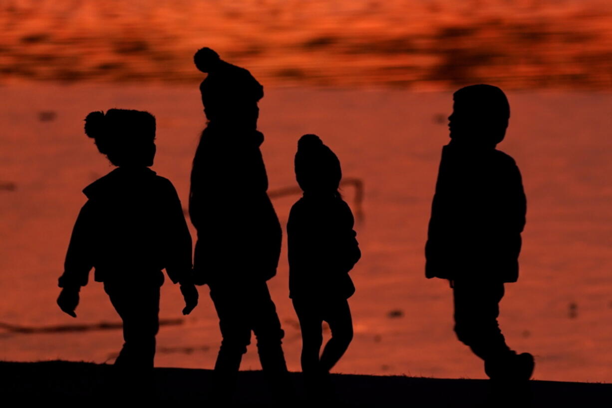 FILE - Kids are silhouetted against a pond at a park in Lenexa, Kan., on Saturday, Dec. 26, 2020. Health officials remain perplexed by mysterious cases of severe liver damage in hundreds of young children around the world. In May 2022, the U.S. Centers for Disease Control and Prevention officials said they are now looking into 180 possible cases across the U.S. More than 20 other countries have reported hundreds more cases in total, though the largest numbers have been in the U.K. and U.S.