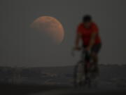 A lunar eclipse is seen behind a cyclist during the first blood moon of the year, in Irwindale, Calif., Sunday, May 15, 2022. (AP Photo/Ringo H.W.