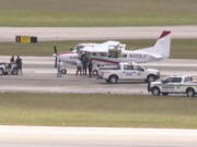 In this still image from video by WPTV shows emergency personnel surrounding a Cessna plane at Palm Beach International Airport Tuesday, May 10, 2022, in West Palm Beach, Fla. A passenger with no flying experience was able to land the plane safely with help of air traffic controllers after the pilot was too sick to handle the controls.