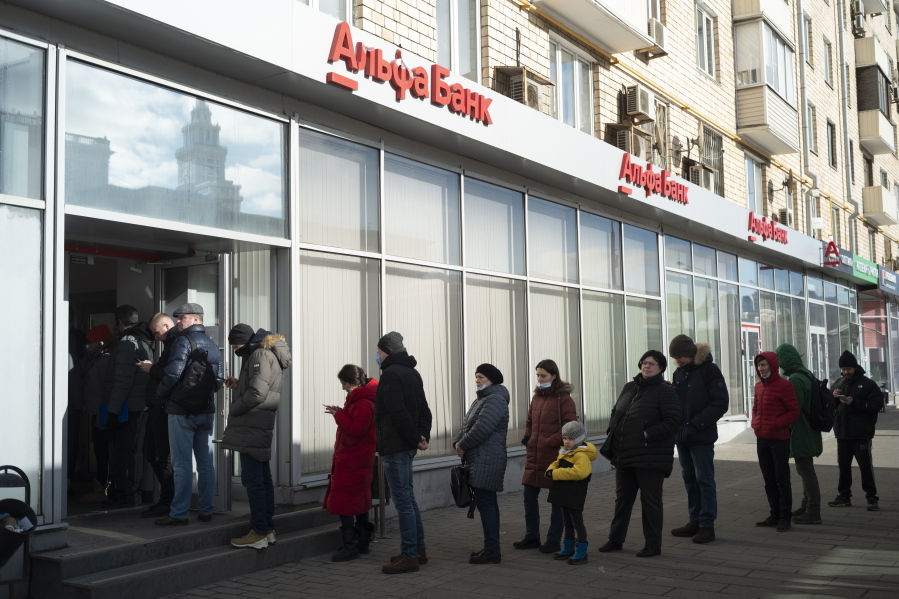 FILE - People stand in line to withdraw money from an ATM of Alfa Bank in Moscow, Russia, Sunday, Feb. 27, 2022. Russians flocked to banks and ATMs shortly after Russia launched an attack on Ukraine on Feb. 24 and the West announced crippling sanctions.