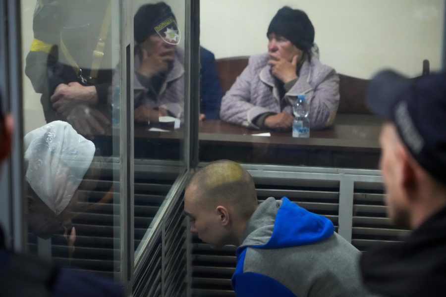 Sitting behind a glass, Russian army Sergeant Vadim Shishimarin, 21, talks with his translator, left, during a court hearing in Kyiv, Ukraine, Wednesday, May 18, 2022. The Russian soldier has gone on trial in Ukraine for the killing of an unarmed civilian. The case that opened in Kyiv marked the first time a member of the Russian military has been prosecuted for a war crime since Russia invaded Ukraine 11 weeks ago.