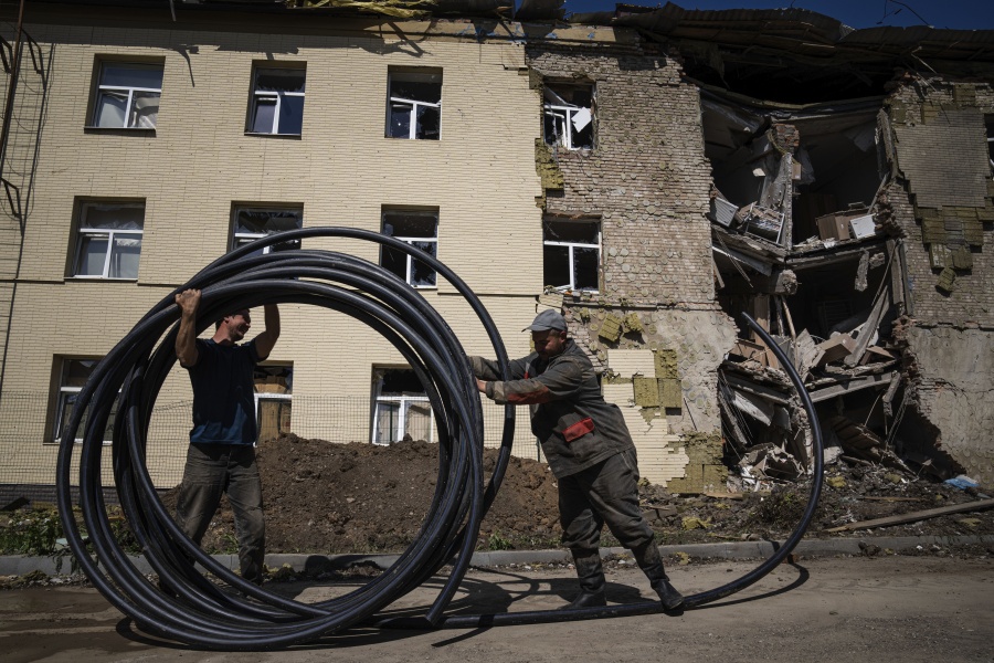 Municipal workers prepare a new tube to restore water supply in front of the building damaged by a Russian attack in Bahmut, Ukraine, on Thursday, May 12, 2022.