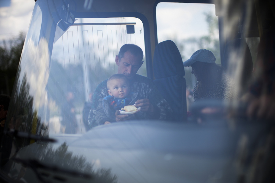 A man feeds a child as they arrive by bus at a reception center for displaced people in Zaporizhzhia, Ukraine, Monday, May 2, 2022. Thousands of Ukrainian continue to leave Russian occupied areas.