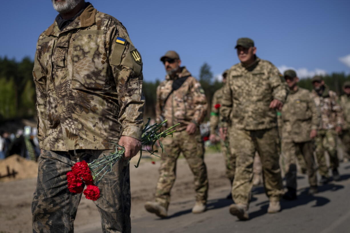 Irpin Territorial Defence and Ukrainian Army soldiers hold flowers to be placed on the graves of comrades fallen during the Russian occupation, at the cemetery of Irpin, on the outskirts of Kyiv, on Sunday, May 1, 2022.