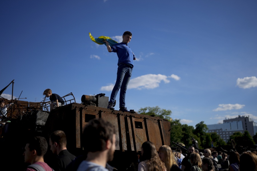 A boy holds a Ukrainian flag on a destroyed Russian tank placed as a symbol of war during Kyiv Day celebrations in downtown Kyiv, Ukraine, Sunday, May 29, 2022. Ukraine's capital celebrates the anniversary of its foundation every last Sunday of May.