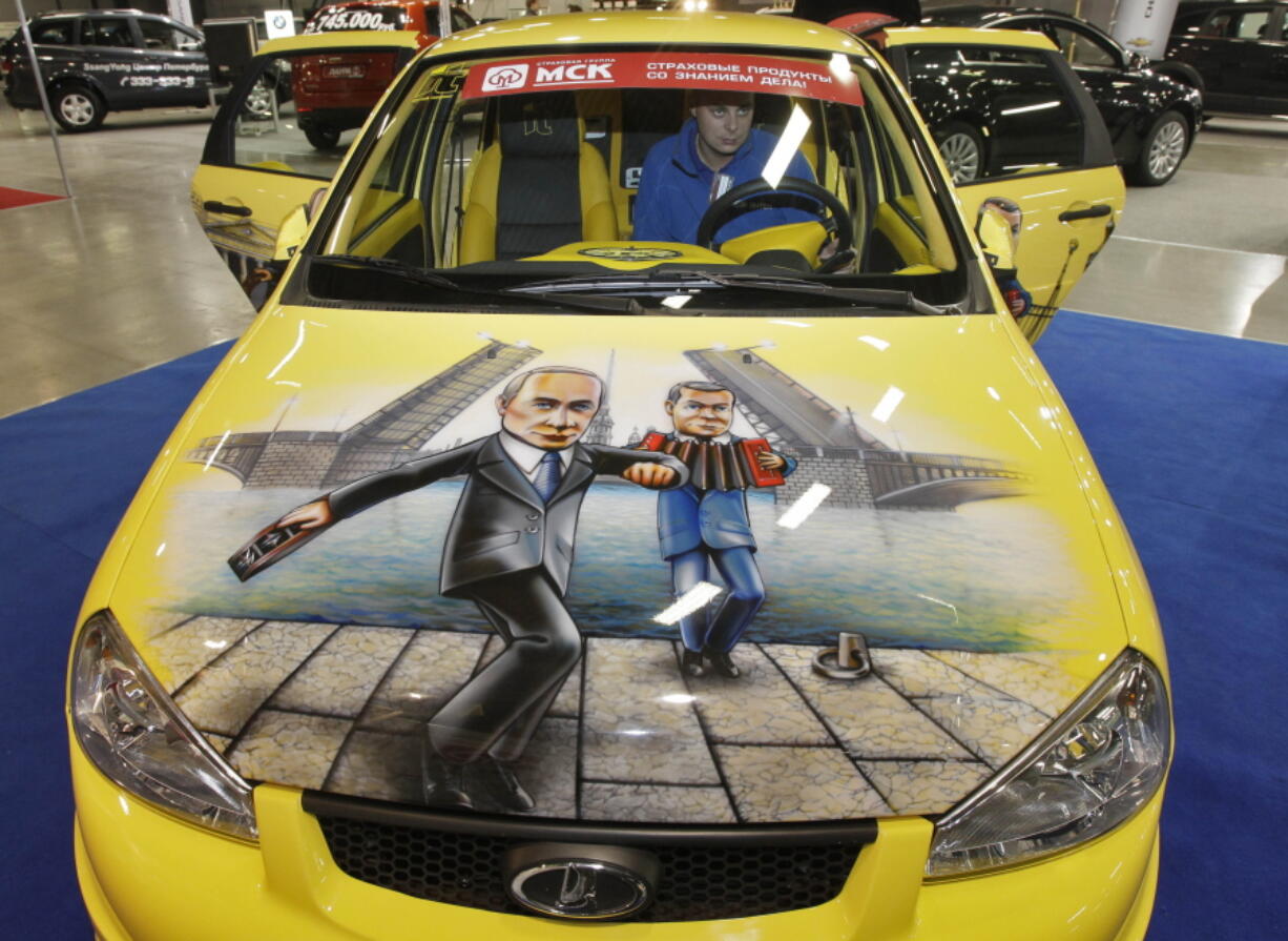 FILE - In this Oct. 21, 2011 file photo, a man sits in a Russian made Lada Kalina sports car with a depiction of Russian Prime Minister Vladimir Putin, left, and Russian President Dmitry Medvedev painted on the bonnet, at a car tuning company's stand during an automotive exhibition in St. Petersburg, Russia. Russia will take control of French car manufacturer Renault's operations in the country and resurrect a Soviet-era auto brand. The news Monday marks the first major nationalization of a foreign business since the war with Ukraine began. Renault says it would sell its majority stake in Avtovaz to a state-run research institute known as NAMI. Avtovaz is best known for its Lada brand.