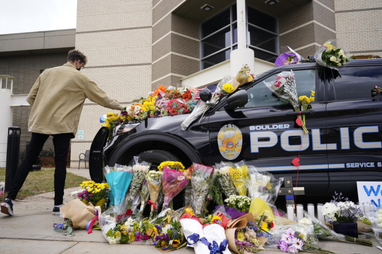 In this March 23, 2021, photo, a man leaves a bouquet on a police cruiser parked outside the Boulder Police Department after an officer was one of the victims of a mass shooting at a King Soopers grocery store in Boulder, Colo. The suspects in the most recent shooting sprees found it relatively easy to get their guns.