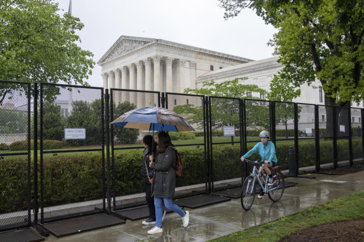 Pedestrians and bikers pass fencing that blocks off the area around the U.S. Supreme Court, Saturday, May 7, 2022, in Washington. A draft opinion suggests the U.S. Supreme Court could be poised to overturn the landmark 1973 Roe v. Wade case that legalized abortion nationwide, according to a Politico report released Monday. Whatever the outcome, the Politico report represents an extremely rare breach of the court's secretive deliberation process, and on a case of surpassing importance.