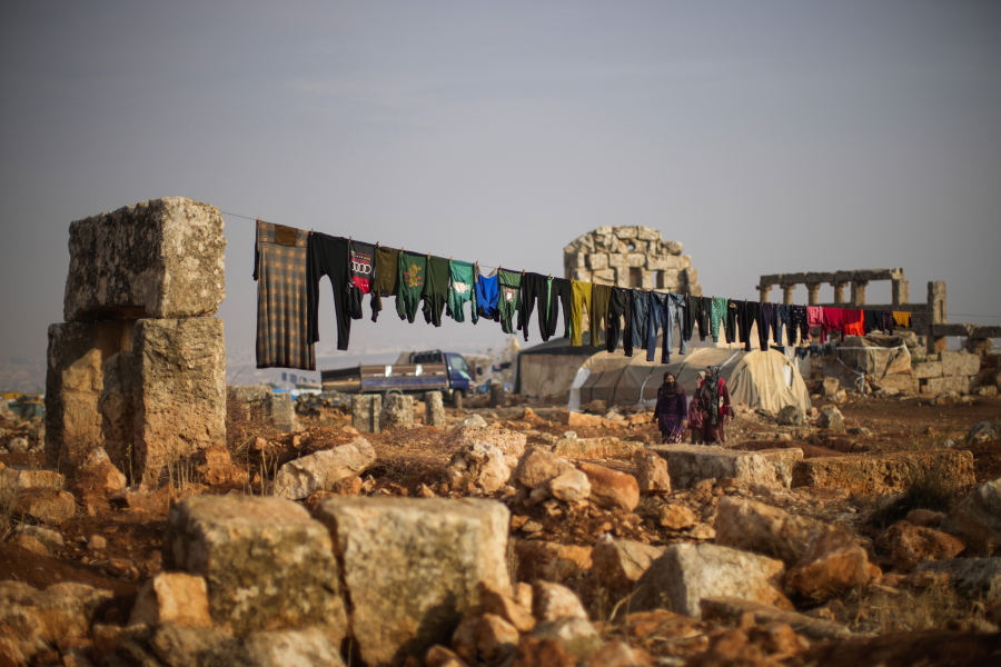 FILE - Syrian displaced people walk next to ancient Roman era ruins where they have set their tends in Sarmada district, north of Idlib city, Syria, Thursday, Nov. 25, 2021.  Fallout from the 2-month-old war in Ukraine is worsening long-term humanitarian crises elsewhere, including in Syria.