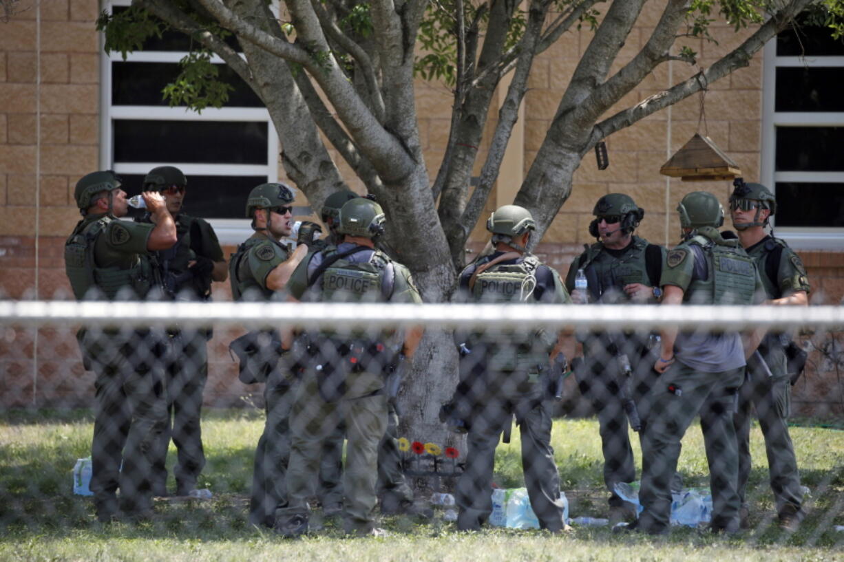 FILE - Law enforcement personnel stand outside Robb Elementary School following a shooting, May 24, 2022, in Uvalde, Texas. When the gunman arrived at the school, he hopped its fence and easily entered through an unlocked back door, police said. He holed himself up in a fourth-grade classroom where he killed the children and teachers.
