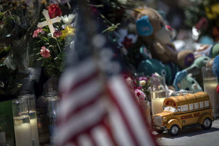 A toy yellow school bus is placed in front of a cross to honor Rojelio Torres, one of the children killed during the mass shooting in Robb Elementary School, while an American flag is seen in the foreground, Sunday, May 29, 2022, in Uvalde, Texas.