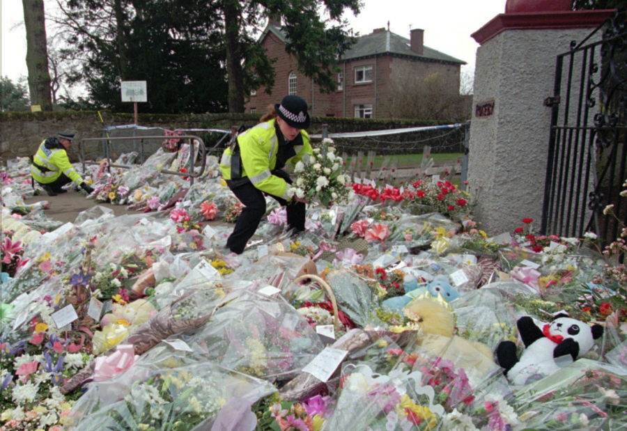 FILE - A police officer arranges bouquets of flowers in rows at a side entrance to Dunblane Primary School in Dunblane, Scotland Friday, March 15, 1996. A 1996 school shooting that killed 16 children in Dunblane was Britain's deadliest school shooting -- and also the only one.