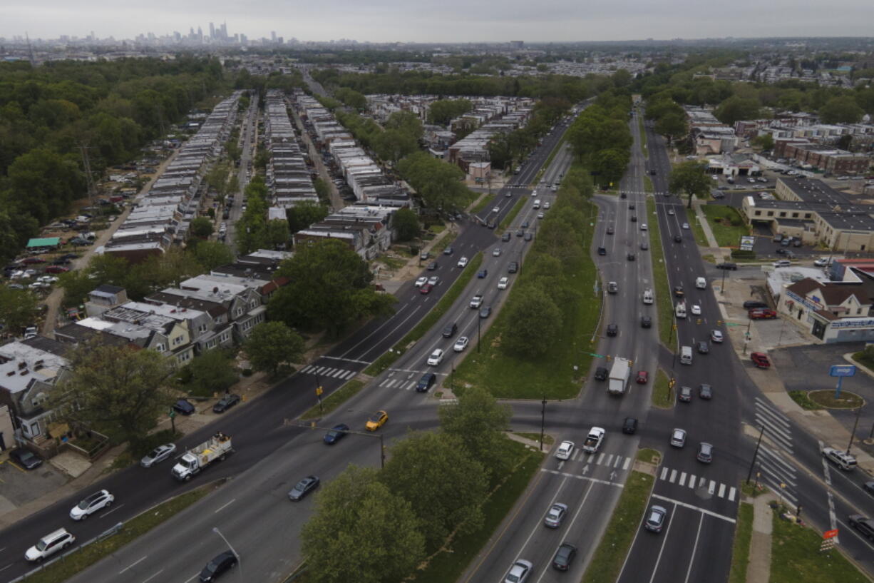 The Philadelphia skyline, top, is seen at a distance as vehicular traffic flows along Roosevelt Boulevard at the intersection with Whitaker Avenue, Thursday, May 12, 2022, in Philadelphia. Roosevelt Boulevard is an almost 14-mile maze of chaotic traffic patterns that passes through some of the city's most diverse neighborhoods and Census tracts with the highest poverty rates. Driving can be dangerous with cars traversing between inner and outer lanes, but biking or walking on the boulevard can be even worse with some pedestrian crossings longer than a football field and taking four light cycles to cross.
