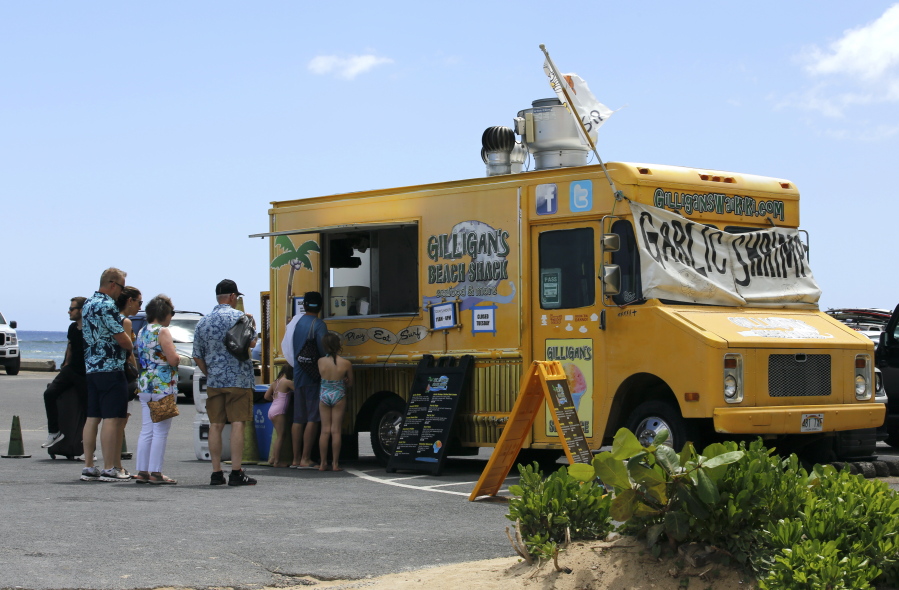 People line up at a food truck parked near Waikiki Beach in Honolulu, Monday, May 23, 2022. A COVID surge is under way that is starting to cause disruptions as schools wrap up for the year and Americans prepare for summer vacations. Case counts are as high as they've been since mid-February and those figures are likely a major undercount because of unreported home tests and asymptomatic infections. But the beaches beckoned and visitors have flocked to Hawaii, especially in recent months.