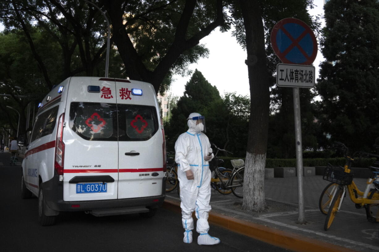 A worker wearing a protective suit to help protect against COVID-19 stands outside an ambulance parked along a street in Beijing, Thursday, May 26, 2022.