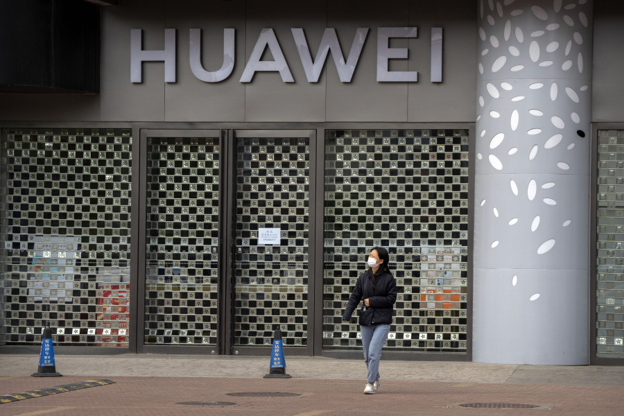 A woman wearing a face mask walks past a Huawei store temporarily closed due to coronavirus-related restrictions in Beijing, Thursday, May 12, 2022. China's leaders are struggling to reverse a deepening economic slump while keeping a "zero-COVID" strategy that has shut down Shanghai and other cities.