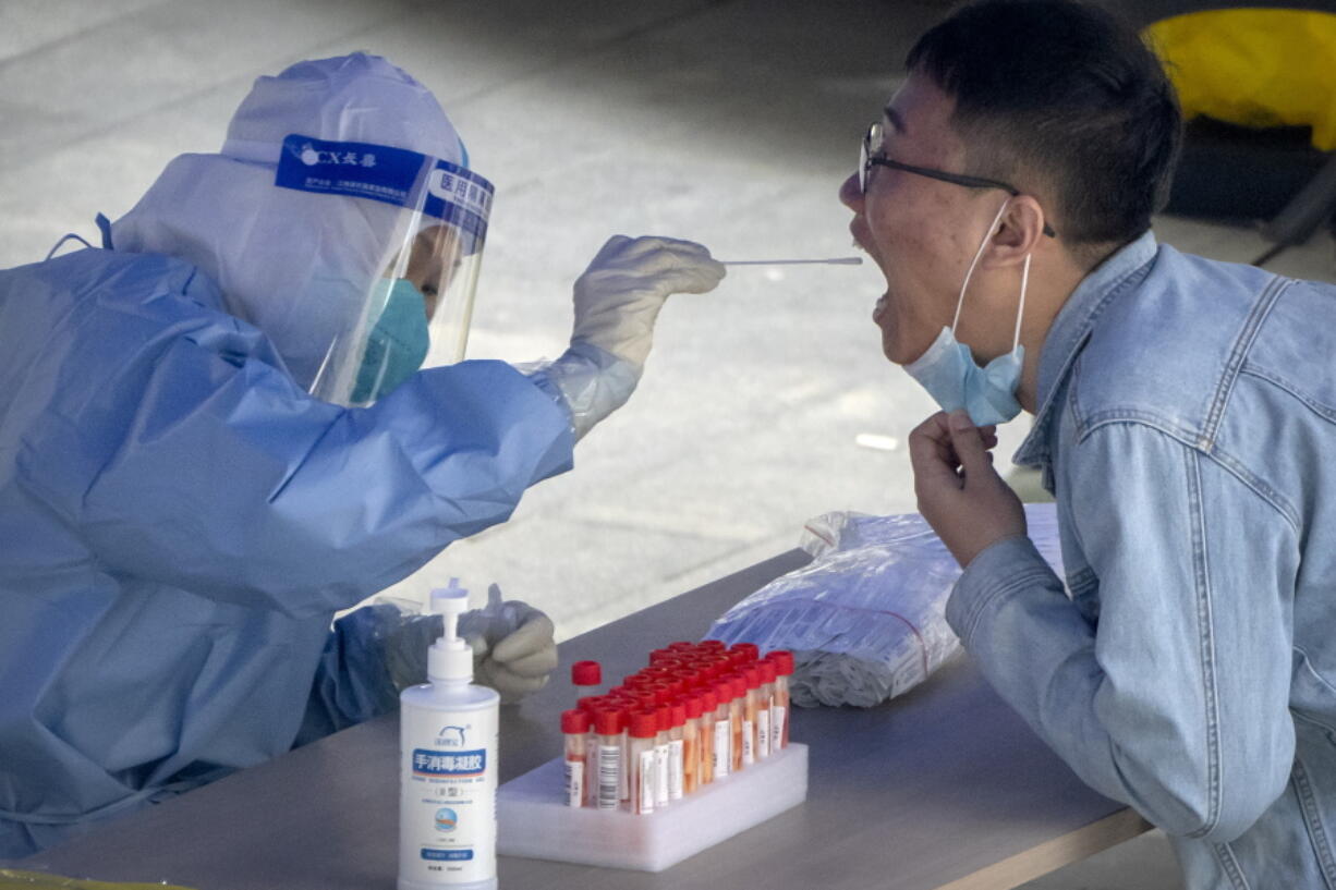 FILE - A worker in a protective suit swabs a man's throat for a COVID-19 test at a testing site in an office complex in Beijing, Friday, April 29, 2022. The World Health Organization on Thursday, May 5, 2022 is estimating that nearly 15 million people were killed either by the coronavirus or by its impact on overwhelmed health systems in the past two years, more than double the official death toll of 6 million.