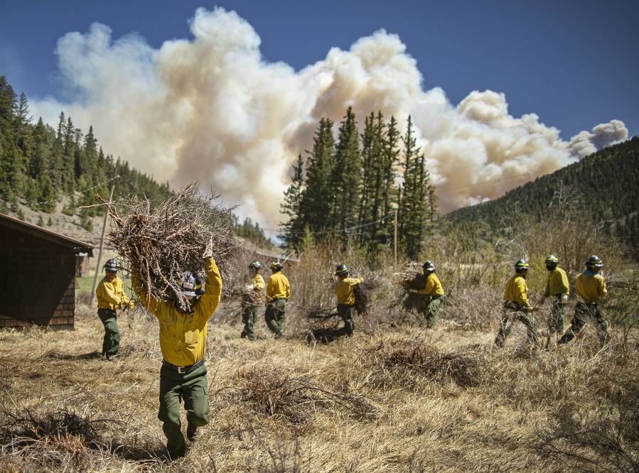 Firefighters with Structure Group 4 clear brush and debris away from cabins along Highway 518 near the Taos County line in New Mexico, May 13, 2022, while fire rages over the nearby ridge.