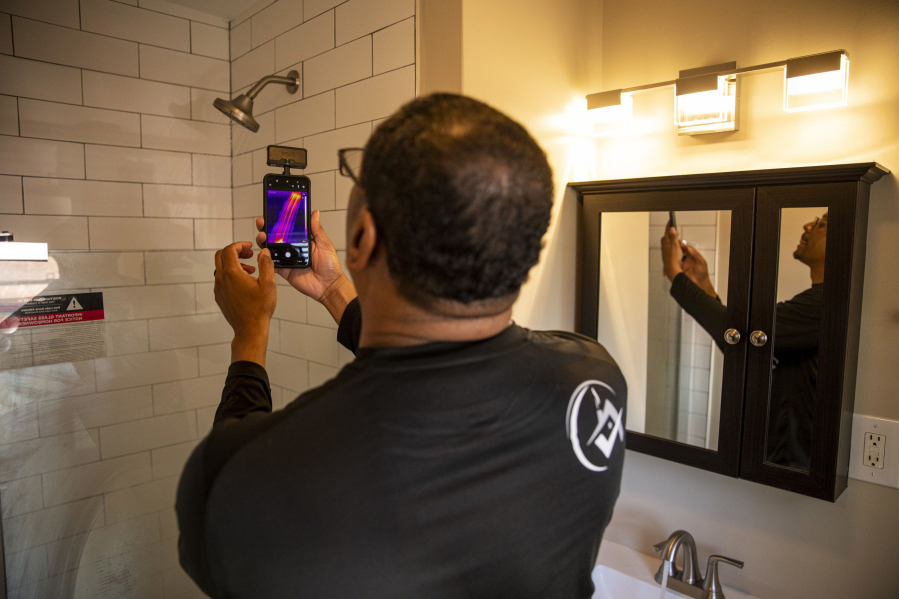 Ben Poles, owner of Rest Assured Inspections, takes a photo and checks the temperature of the water in the shower during a home inspection.