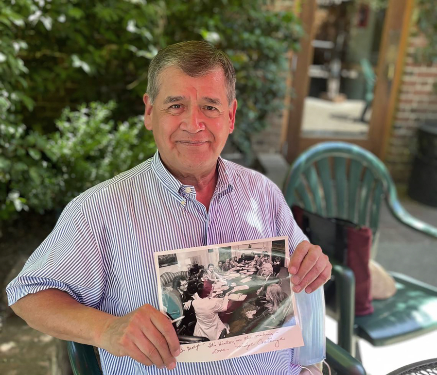 George Raya is pictured on Thursday, June 9, 2022 in Sacramento. The 73-year-old sits at the Old Soul at The Weatherstone cafe and holds a 1977 photo of himself an the other participants in the National Gay Task Force at the White House.