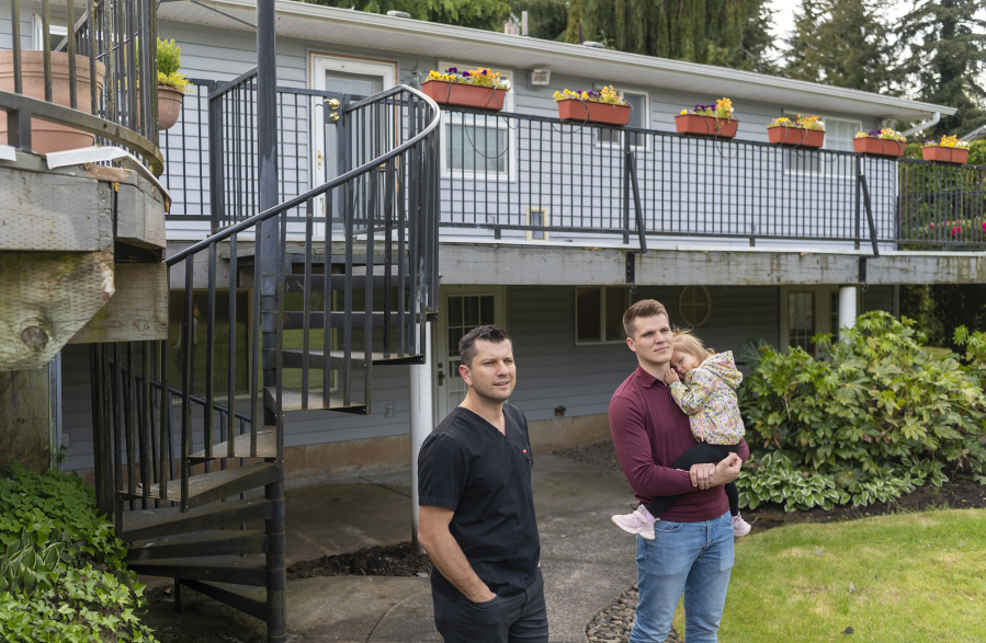 Vadim Zalyashko, left, of Vancouver, stands with Sergey Kushnarenko and Kushnarenko's 2-year-old daughter, Ellen, outside their home in Vancouver. Kushnarenko and his family are refugees from the war in Ukraine. Zalyashko and other members of The Father's House Church in Vancouver helped bring the Kushnarenko family to Vancouver by providing them a home and other resources.
