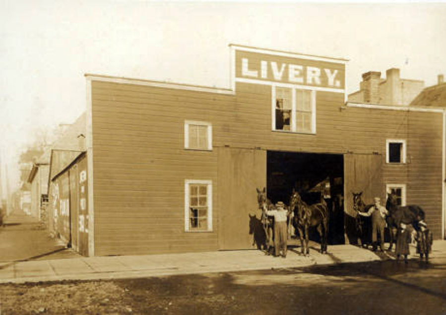 John Crass (in white shirt) stands near a helper, each holding two horses at a livery stable at 214 West Fourth St. in Vancouver. Besides horse and buggy rentals, livery stables were often a sort of community center offering after-hours entertainment from bawdy performances to pugilistic combat. During the day, they proved a reliable source for county gossip and rumors.