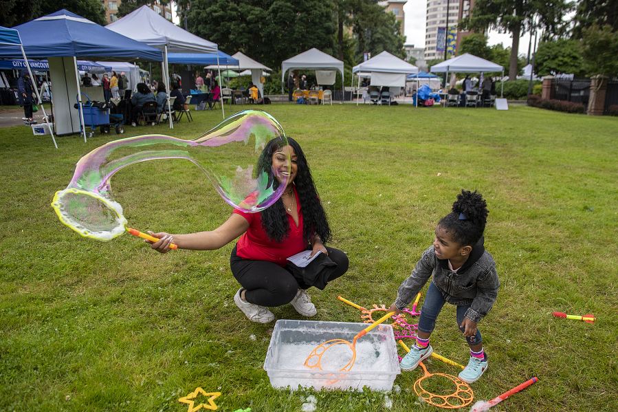 Aiyana Thomas, a volunteer with the city of Vancouver, left, is all smiles while joining Illianna Harris, 3, of Vancouver as they play with bubbles Friday afternoon during the Juneteenth Freedom Celebration at Esther Short Park. The event featured food, live music, art, informational booths and traditional games.