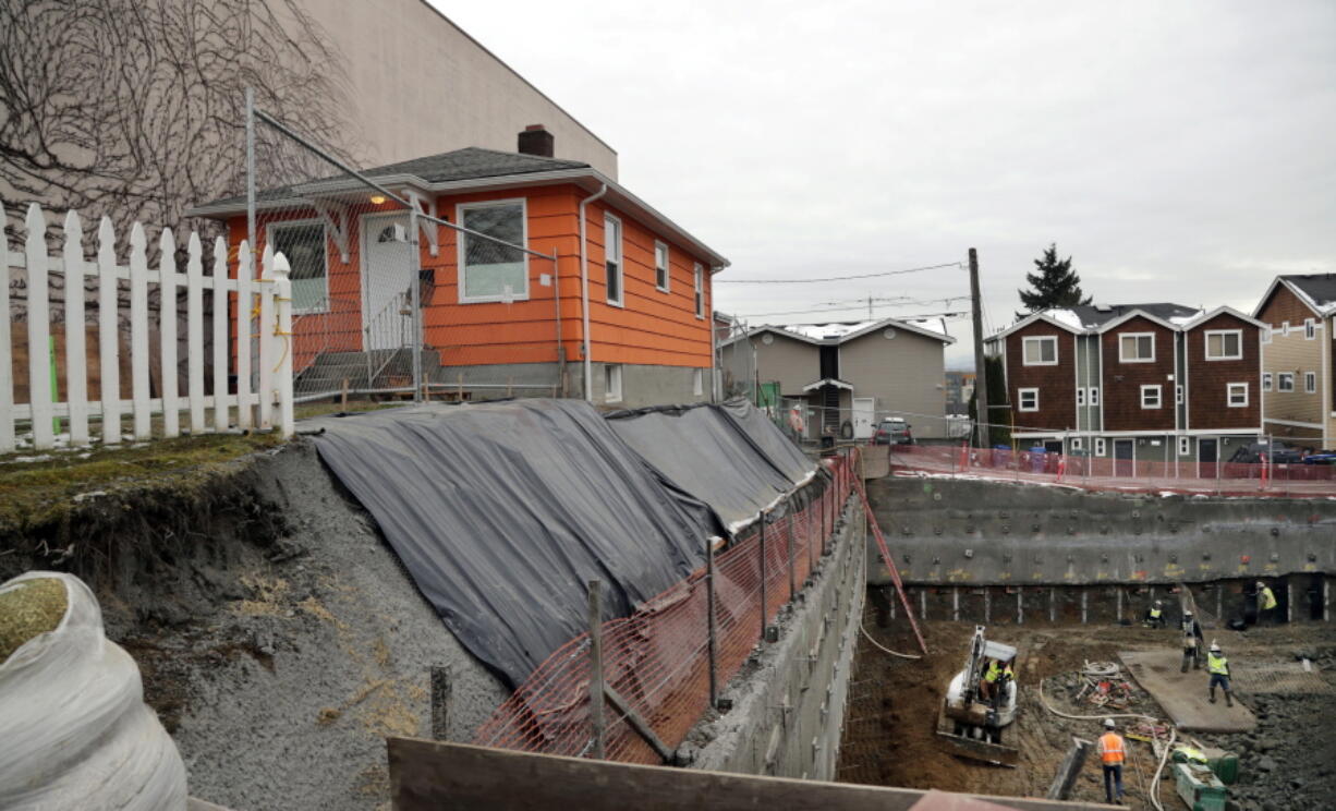 FILE - In this Dec. 27, 2017, photo, a single-family home remains on the edge of where a multi-story, mixed-use building is being constructed in Seattle. Amazon said Thursday, June 23, 2022, it will provide $23 million to help minority-led organizations build or preserve more than 500 new affordable housing units in Seattle -- the latest spending by a tech company to ease a severe housing crunch the industry has helped create.