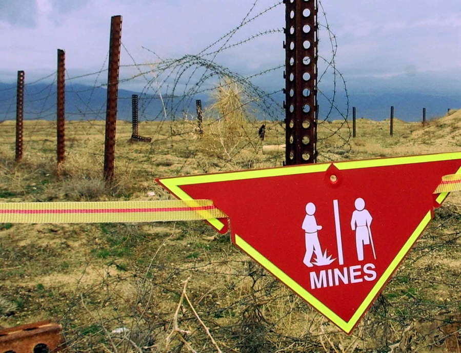 FILE - An international sign warning about mines hangs beside a minefield at Bagram Air Base on, March 22, 2002. The White House announced Tuesday a new policy curtailing the use of anti-personnel land mines by the U.S. military, reversing a more permissive stance that was enacted by former President Donald Trump. Under the policy, such explosives will still be allowed to defend South Korea against a potential attack by North Korea, but otherwise they will be banned.